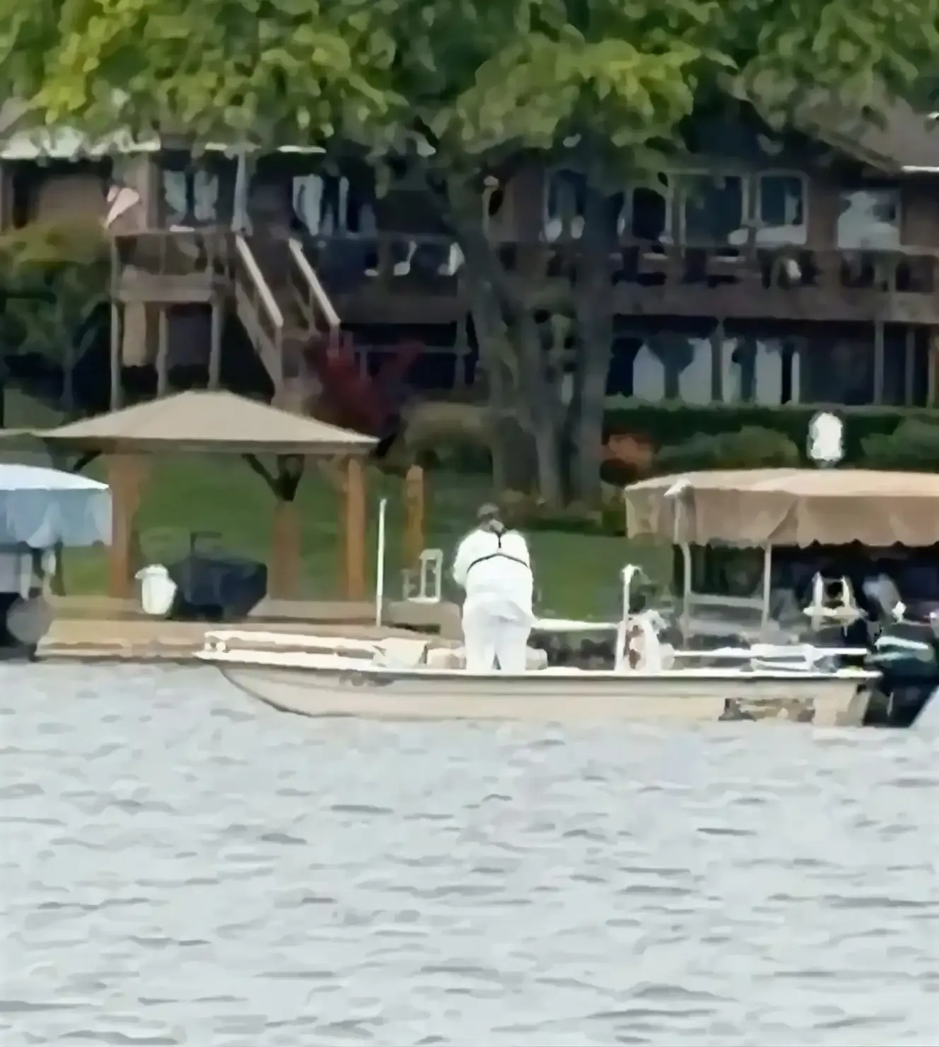 An applicator in protective gear treating vegetation from a boat near a dock