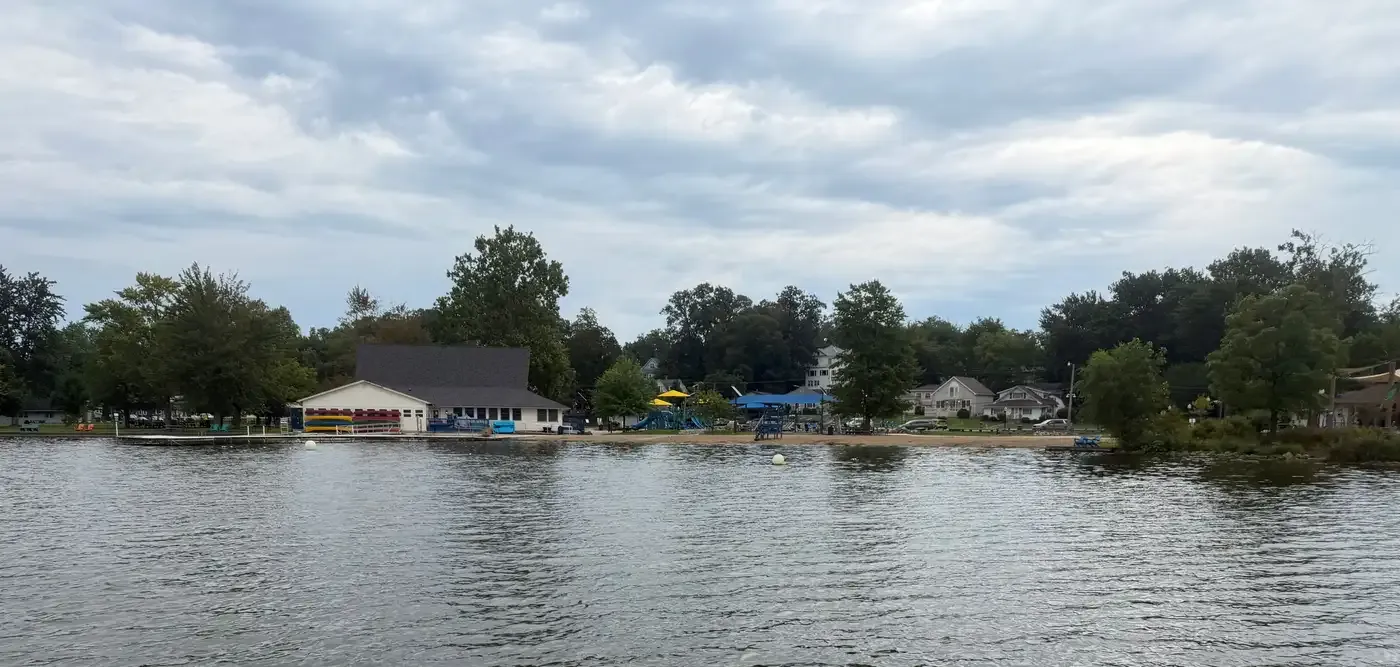The Limitless Park beach and swim area seen from the water, with the boathouse, kayak racks, and playground along the shore