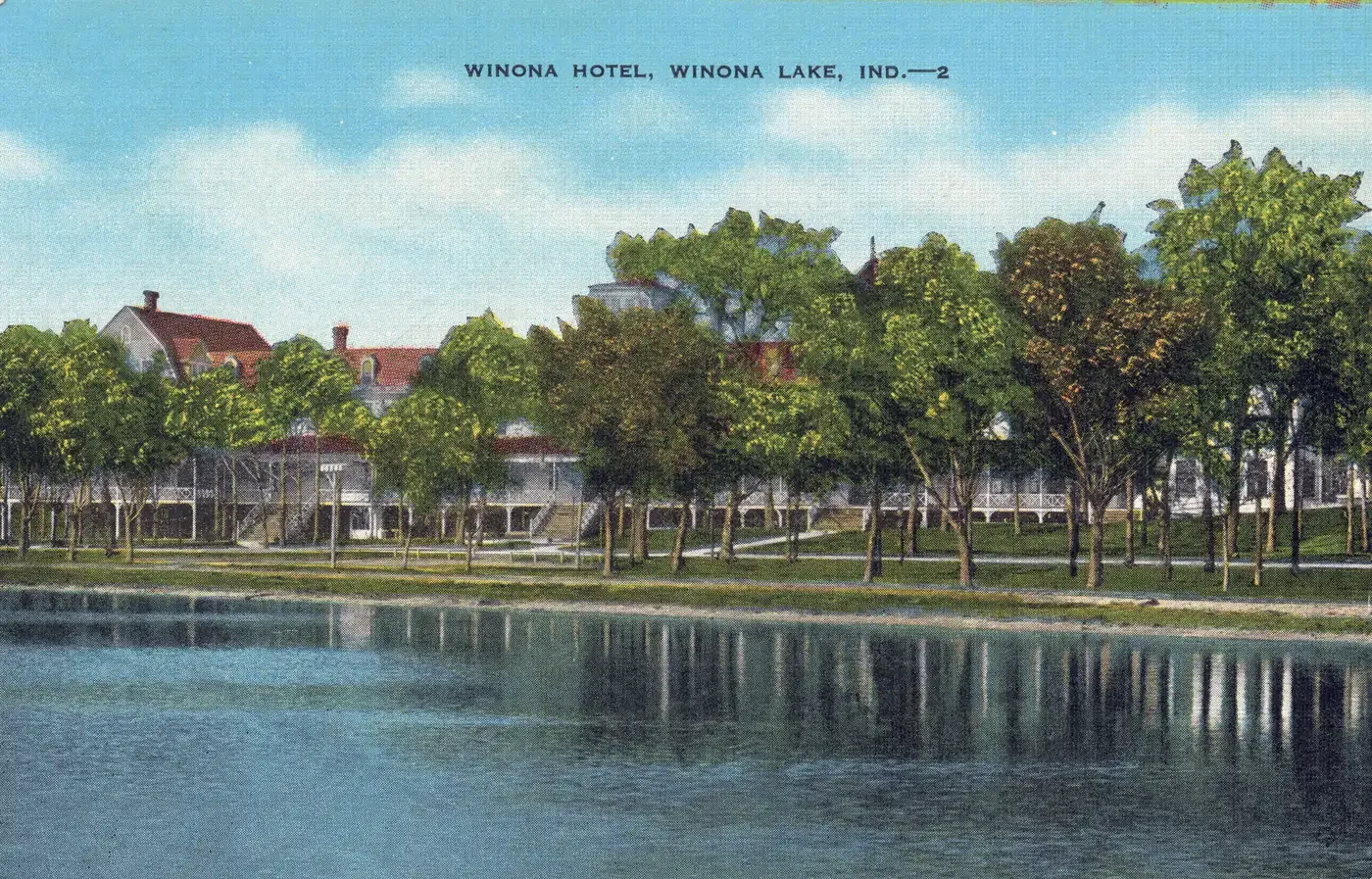 A linen postcard of the Winona Hotel seen across the water, a long white three-story building with porches behind a row of shoreline trees under a blue sky, titled Winona Hotel, Winona Lake, Ind.