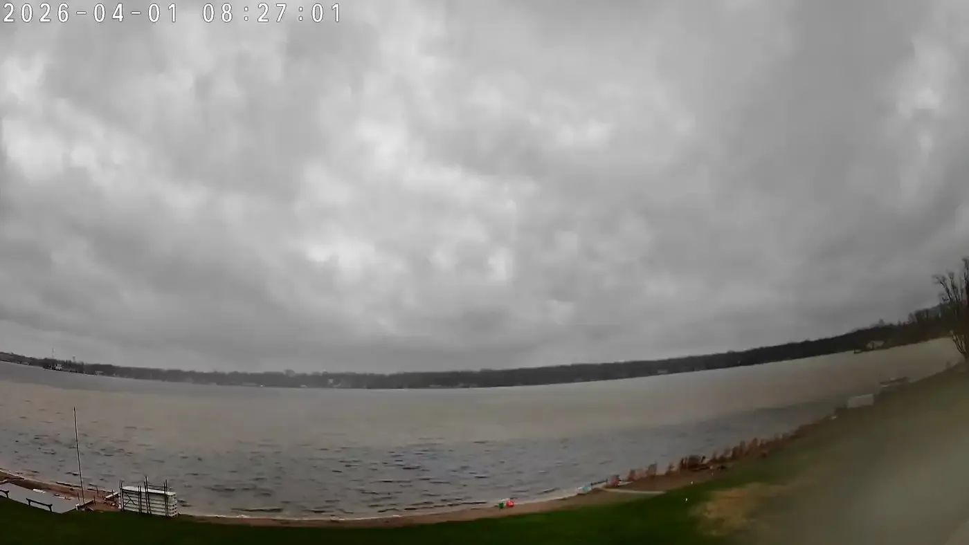 Turbid brown runoff water spreading along the Winona Lake shoreline under a gray sky