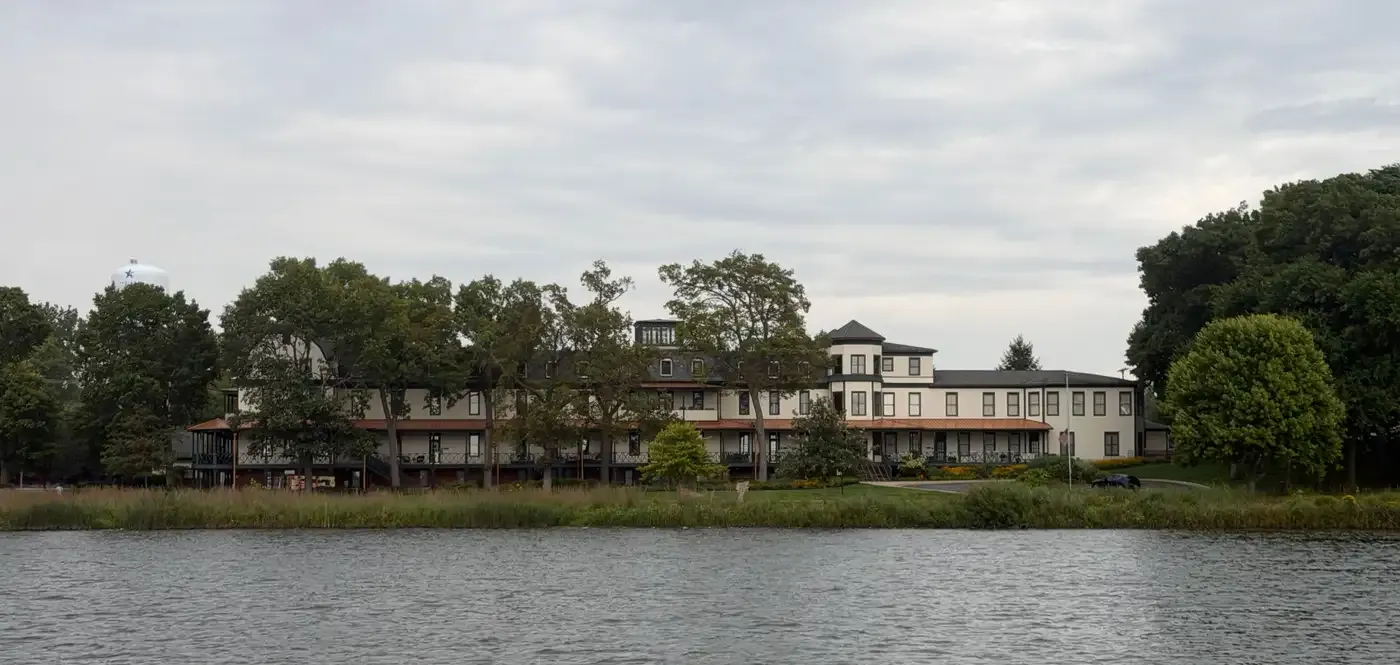 The Winona Hotel seen from the lake, a long white three-story building with covered porches behind shoreline trees
